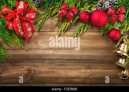 Disposizione di natale con rami di conifere, rosso archi e baubles, pigne e oro campane confinanti con un legno rustico plance indietro Foto Stock