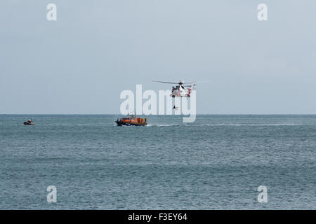 H.M Coastguard salvataggio elicottero abbassamento winchman a RNLI linshore scialuppa di salvataggio, lavorando insieme per l'esercizio al largo dell'isola di wight Coast, regno unito Foto Stock