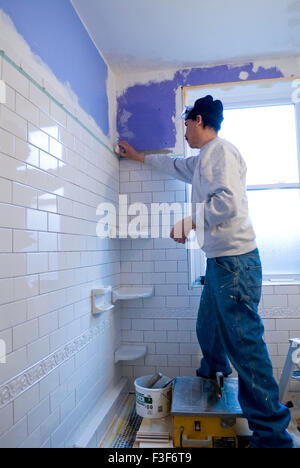 Uomo messicano tiling un muro di una stanza da bagno con piastrelle di metropolitana. Foto Stock