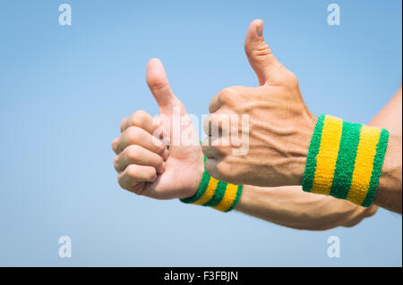 Il brasiliano atleta che indossa i colori del Brasile di braccialetti tenendo due pollici in su contro il cielo blu Foto Stock