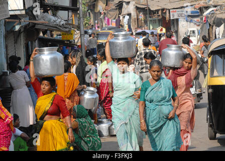 Le donne portano acqua potabile in contenitori di alluminio sulle loro teste in una delle baraccopoli in Chembur ; Bombay ora Mumbai ; Maharashtra ; India Foto Stock