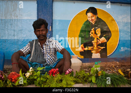 Uomo che vendono fiori nella parte anteriore di un dipinto raffigurante Jayalalithaa, il Primo Ministro del Tamil Nadu (India) Foto Stock