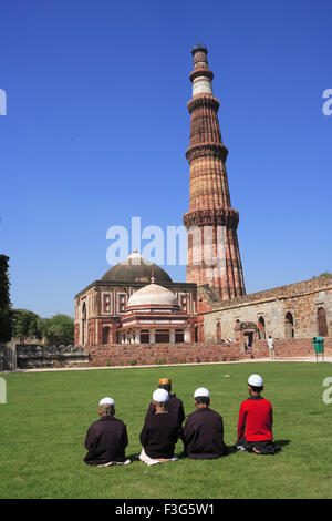 I bambini facendo Namaz davanti Alai Darwaza ; Imam Zamin la tomba e Qutab Minar pietra arenaria rossa torre Indo arte musulmana ; Delhi Foto Stock