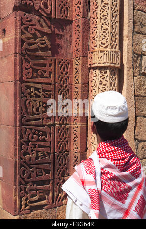 Ragazzo musulmano guardare ornamento islamico Corano iscrizione scolpita Qutab Minar complesso di arenaria rossa torre Indo musulmano Delhi Foto Stock