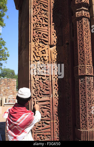 Ragazzo musulmano guardare ornamento islamico Corano iscrizione scolpita Qutab Minar complesso di arenaria rossa torre Indo musulmano Delhi Foto Stock