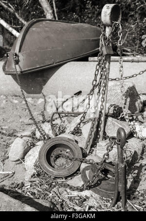 Vecchio rosso canotto giace sulla costa vicino arrugginita ancore e catene, dai toni monocromatici foto, uno stile rétro Foto Stock