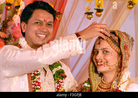 South Asian indù indiano gujarati matrimonio ; sposo mettendo sindoor sulla testa di sposo con volto sorridente mostra Mumbai Foto Stock