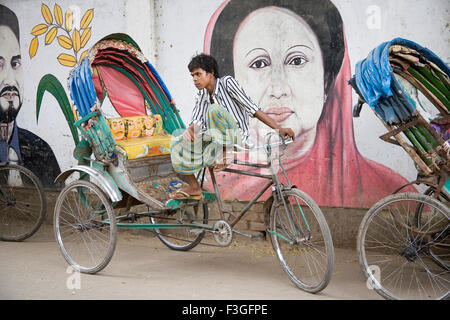 In rickshaw estrattore di attesa per il passeggero vicino al muro dipinto del candidato iniziata Khalida Zia vecchia Dacca in Bangladesh Foto Stock