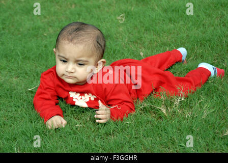 Indian baby boy in abito rosso strisciando gioca su erba verde - mrr#152 - 135897 rmm Foto Stock