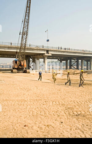 Lavoratori edili manualmente il trasporto di barre di ferro in un cantiere sul fiume Sabarmati ; Ahmedabad ; Gujarat ; India Foto Stock