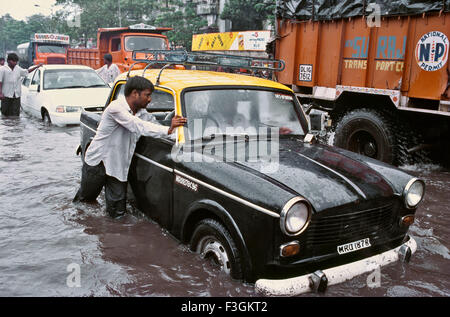 Conducente spingendo il suo filamento taxi su una strada allagata durante il monsone pesante ; Bombay ora Mumbai ; Maharashtra ; India Foto Stock