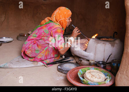 Indiano donna Rajasthani soffiando attraverso il tubo sul fuoco di cottura degli alimenti ; Jodhpur ; Rajasthan ; India Foto Stock