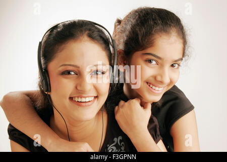 Maharashtrian ragazza adolescente ascoltare la musica tramite auricolari di undici anni Gujarati ragazza abbracciando il suo da dietro MR686M;191 Foto Stock