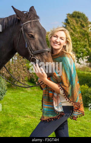 Bella donna felice che indossa il poncho, sorridente e portando il suo cavallo nella luce del sole Foto Stock