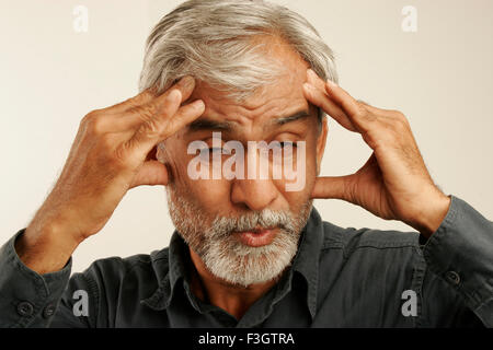Indian vecchio uomo tardi anni cinquanta capelli grigi indossando maglietta blu che esprime grave cefalea premendo sulla fronte le dita delle mani irritato Foto Stock