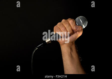 Maschio di mano che tiene il microfono con cavo di filo isolato su sfondo nero Foto Stock