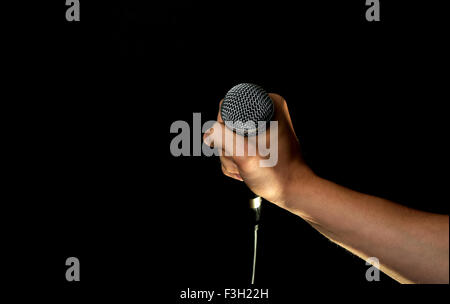 Maschio di mano che tiene il microfono con cavo di filo isolato su sfondo nero Foto Stock