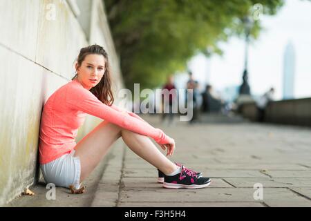 Ritratto di giovane donna seduta runner lungo il fiume Foto Stock