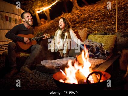 Coppia giovane accanto al fuoco e yurta di cantare e suonare la chitarra Foto Stock