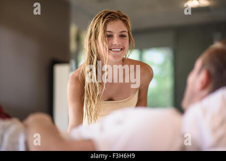 Sulla spalla vista della giovane donna avvolta in asciugamano guardando il fidanzato a letto Foto Stock