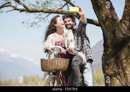 Coppia giovane prendendo selfie dello smartphone in bicicletta nel paesaggio rurale Foto Stock