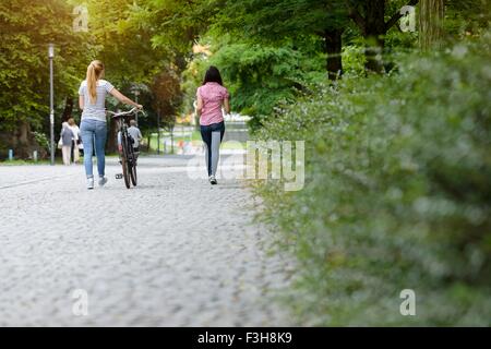 Lunghezza piena vista posteriore delle donne a camminare con la bicicletta Foto Stock