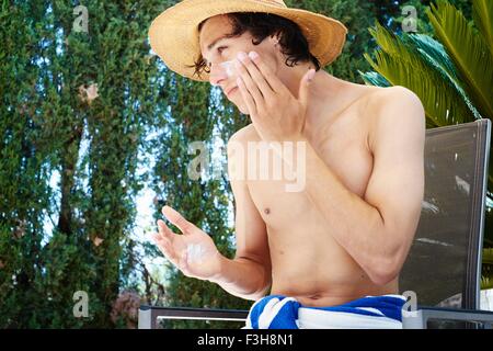 Giovane uomo che indossa cappello l'applicazione di crema solare a faccia Foto Stock