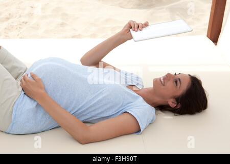 Gravidanza metà donna adulta che giace sulla spiaggia di dormeuse cercando fino a tavoletta digitale Foto Stock