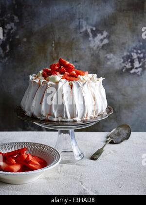 Fragole coperte pavlova sulla torta di vetro stand con server di torta e una ciotola di fragole Foto Stock