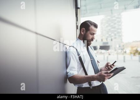 Elegante imprenditore utilizza lo smartphone e tablet digitale al di fuori ufficio Foto Stock