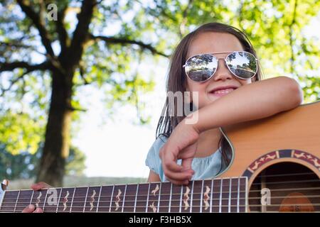 Ragazza con occhiali da sole in posa con la chitarra acustica in posizione di parcheggio Foto Stock