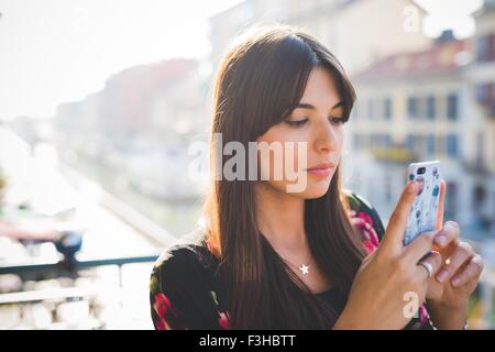 Giovane donna la lettura di testi di smartphone sul balcone fronte mare Foto Stock