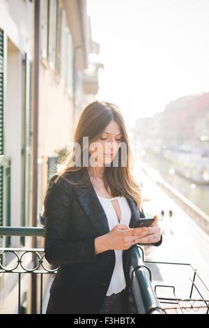 Giovane donna la lettura di testi di smartphone sul balcone fronte mare Foto Stock
