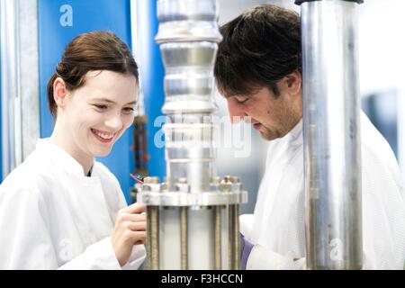 Maschio e femmina colleghi indossando camici da laboratorio utilizzando attrezzature scientifiche, guardando verso il basso sorridente Foto Stock