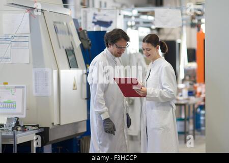 Maschio e femmina colleghi indossando camici da laboratorio guardando appunti sorridente Foto Stock