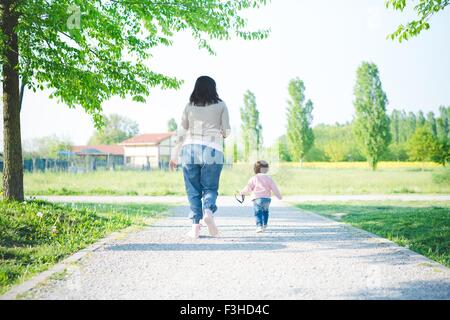 Vista posteriore del toddler femmina toddling con la madre in posizione di parcheggio Foto Stock