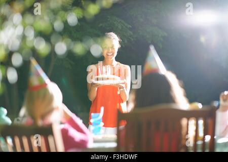 La madre che porta la torta di compleanno al tavolo in giardino festa di compleanno Foto Stock