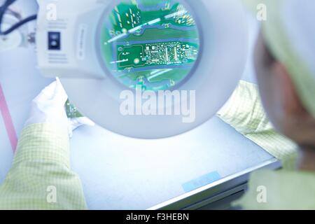Giovane donna magnifier controllo qualità vicina fabbrica di produzione flessibile di schede a circuito elettronico Foto Stock