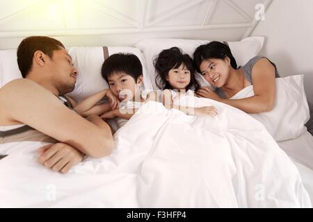 Giovane famiglia cinese di genitori e due figli piccoli che stabilisce nel letto insieme a casa Foto Stock