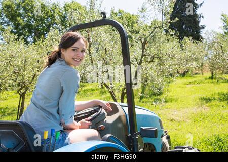 Giovane donna seduta del trattore guardando sopra la spalla alla fotocamera a sorridere Foto Stock