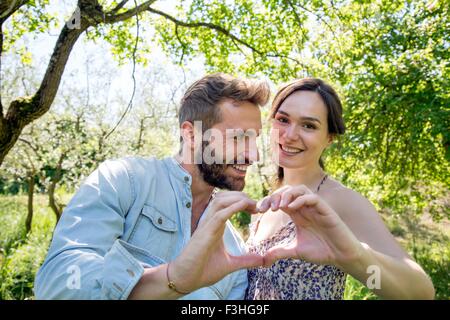 Coppia giovane messa a forma di cuore con le mani, guardando alla fotocamera a sorridere Foto Stock