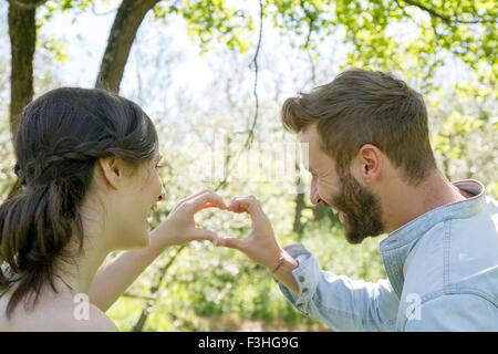 Vista posteriore della coppia giovane messa a forma di cuore con le mani Foto Stock