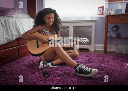 Ragazza seduta sul pavimento della camera a suonare la chitarra che guarda lontano sorridente Foto Stock