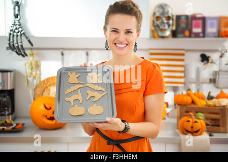 Felice giovane massaia tenendo il vassoio di crudo biscotti di Halloween. Halloween considera pronta per andare in forno. Tradizionale autunno vacanza. Foto Stock