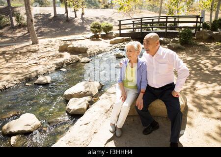 Coppia senior seduto sulla roccia accanto a stream Foto Stock