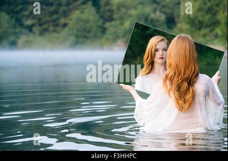 Vista posteriore della giovane donna in piedi nel lago Specchio di contenimento guardando la riflessione Foto Stock