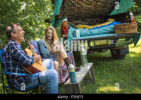 Uomo maturo di cantare e suonare la chitarra acustica per la ragazza mentre camping Foto Stock