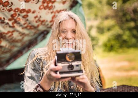 Ritratto di giovane donna fotografare con fotocamera istantanea mentre camping Foto Stock