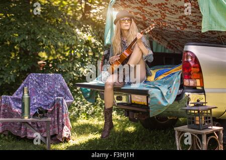 Giovane donna giocando ukulele mentre campeggio a prelevare il boot Foto Stock