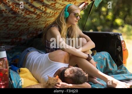 Giovane donna che indossa le cuffie con il mio ragazzo nel pick up boot mentre camping Foto Stock